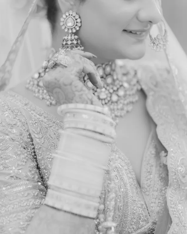 Black and white detail of a bride's earring, bangles and hennaed hand.