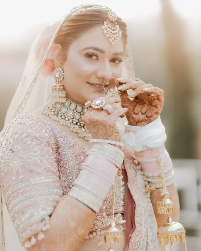 Close portrait of a bride in blush and kundan jewellery, smiling at the camera.