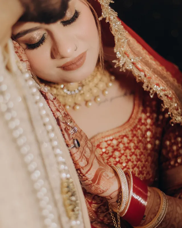 A bride in red and gold looking down, her veil edged with gold beadwork.